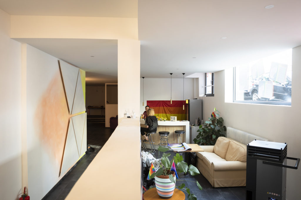 Das Bild zeigt Einblicke in das Inside:out. Im Hintergrund sitz Mosche an der Theke. Man sieht eine Couch, Pflanzen und dreieckige Wandpanele.