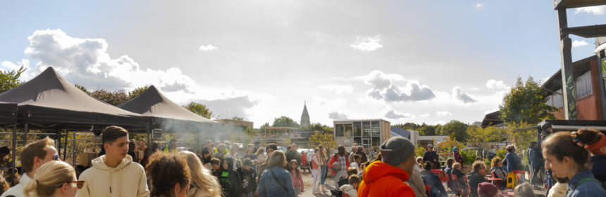 Menschen stehen vor der Alten Glaserei und unterhalten sich, während im Hintergrund der blaue Himmel und die Silhouette der Friedhofskirche zu sehen ist